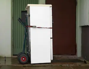 An old fridge strapped in a dolly in front of a Portland OR home